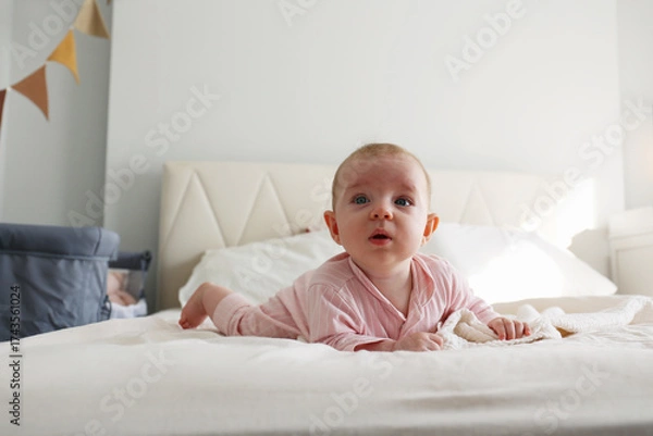 Fototapeta Playful baby learning to crawl on the bed. Copy space, background.