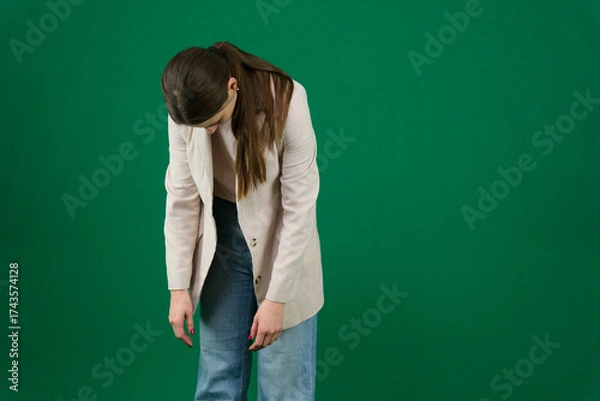 Fototapeta Professional photo collection of young European woman in light blazer with hair tied in ponytail and blue jeans on green chroma key background expressing different emotions and gestures perfect for ad