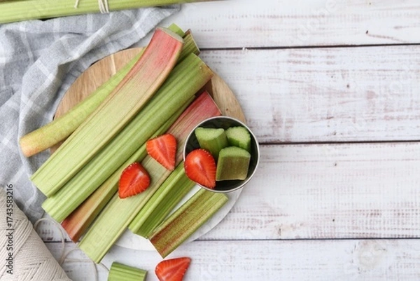 Fototapeta Rhubarb stalks and strawberries on white wooden table, flat lay. Space for text