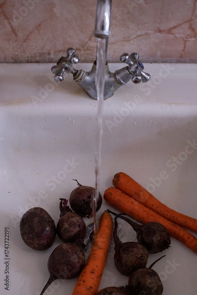 Fototapeta Freshly harvested vegetables washed under running water in a rustic kitchen sink, capturing a vibrant farm-to-table moment