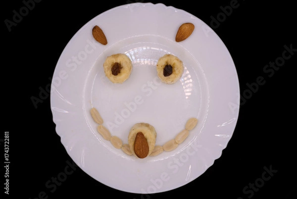 Fototapeta Creative dessert art made with fruits and nuts on a white plate, creating a cheerful face for kids to enjoy during snack time