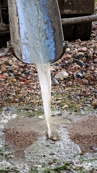 Fototapeta Water flows down the chute of a concrete mixer. Washes the concrete mixer after use. Washing away the remaining cement mixture. Cleaning of special vehicles. Dirty water. Construction site. Vertical.