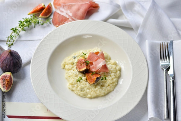 Fototapeta risotto with figs and ham in a white plate on the table