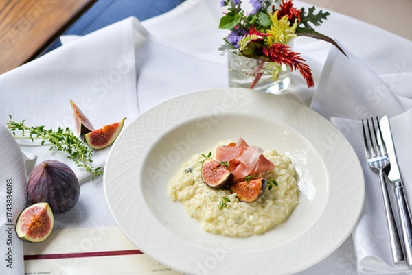 Fototapeta risotto with figs and ham in a white plate on a table with food decor
