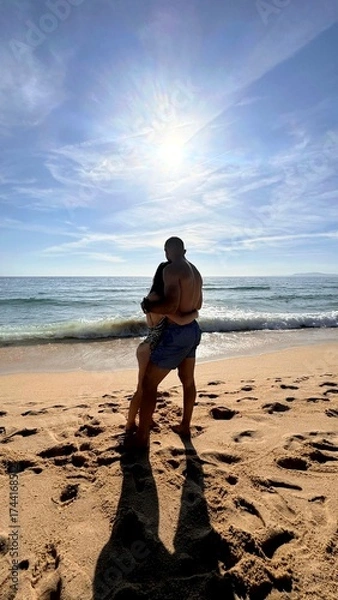 Fototapeta Inlove couple looking at the ocean. Romantic picture of a couple. Beach day on vacation. hugging couple. romantic picture. Beach destination in Europe. 