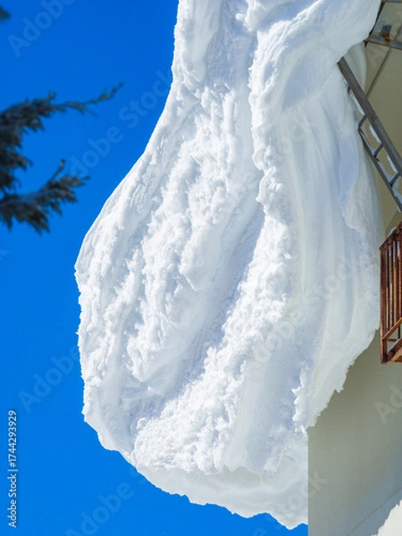 Fototapeta A close-up view of a massive snow cornice on a roof against a clear blue sky (Shiga Kogen, Nagano, Japan)