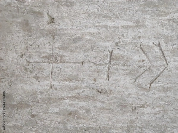 Fototapeta An arrow symbol is carved into a rough stone surface. The markings appear weathered, suggesting age and history.