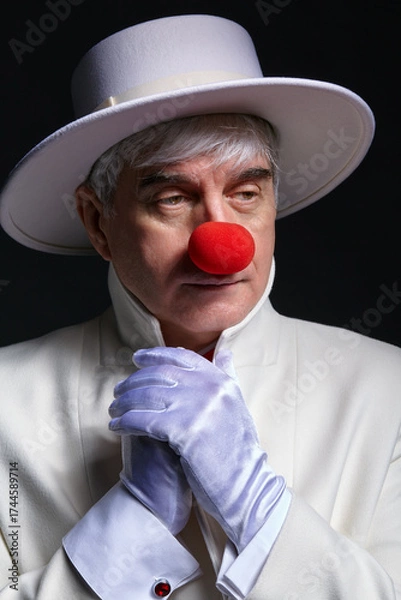 Fototapeta Close-up portrait of sad clown. An elderly man in a white coat and hat.