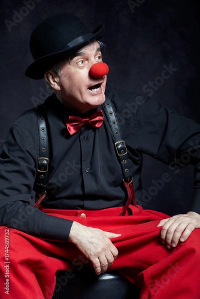 Fototapeta Portrait of a clown on dark background  with red clown nose and bowler hat on head.