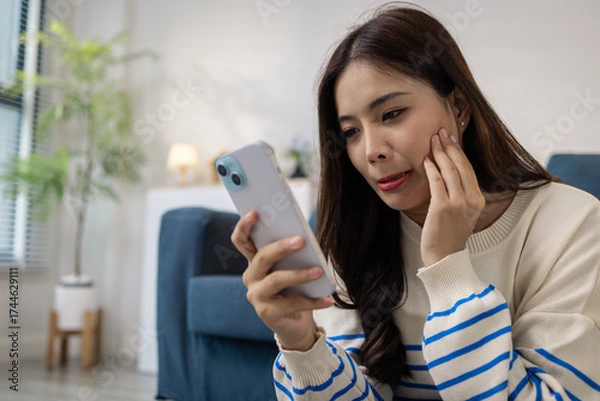 Fototapeta A young woman sits on the floor with a cushion, smiling happily while using her smartphone. She appears relaxed and joyful, enjoying leisure time at home with positive energy.