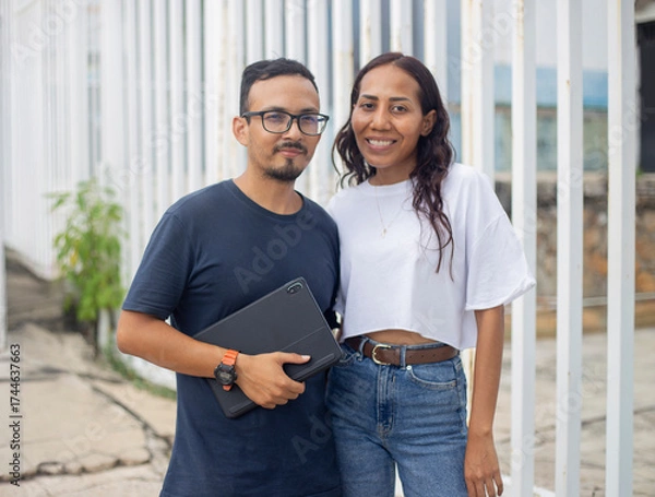 Fototapeta Pareja de jóvenes con tableta en mano con ropa casual 