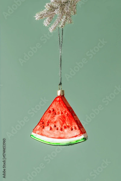 Fototapeta Minimal creative Christmas holidays concept. Red green slice of watermelon hanging on xmas snowy fir tree branch on green. Winter seasonal still life with Christmas decoration, New Year modern design