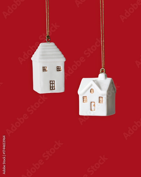 Fototapeta Minimal winter composition with two white ceramic house ornament hanging on red background. Simple Christmas decoration symbolizing home, warmth and holiday coziness. New Year colored Christmas decor.