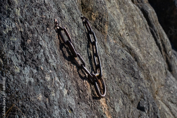 Fototapeta rustic metal chain anchor fixed into rugged rock surface, providing secure point for climbing equipment, symbolizing safety, adventure, and outdoor recreation. close up.