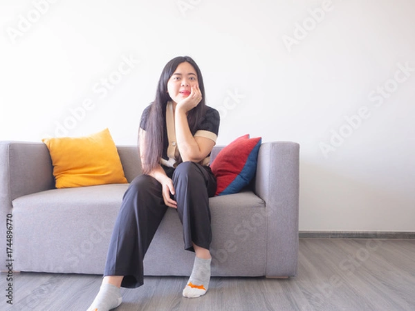 Fototapeta Young woman sits on sofa hugging cushion, smiling and relaxing. Simple pleasures at home concept.
