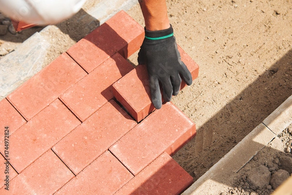 Fototapeta Close-up of Worker laying red paving bricks on newly constructed pathway