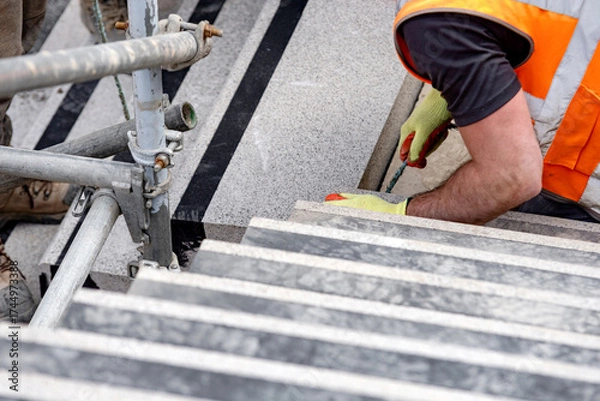 Fototapeta Builders working on construction site to install concrete blocks on stairs to perfect levels according to tolerances