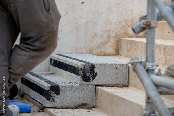 Fototapeta Builders working on construction site to install concrete blocks on stairs to perfect levels according to tolerances
