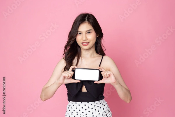 Fototapeta Cheerful smiling Asian woman holding smartphone isolated on pink background.with clipping path