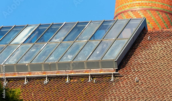 Fototapeta glass roof structure with skylight panels on an old tiled industrial building and a red brick chimney in sunlight