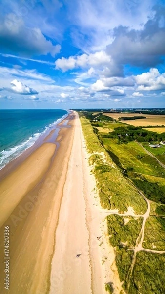 Fototapeta Coastal panorama, aerial view of a wide, sandy beach stretching towards the horizon.  Pale sand meets turquoise ocean water, interspersed with dunes and vegetation.  A clear sky with scattered clouds