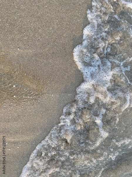 Fototapeta Gentle ocean waves lapping against sandy shore in soft light during a peaceful afternoon