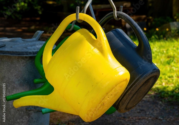 Fototapeta colorful plastic watering cans hanging on metal hooks in sunlight in a garden