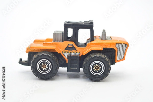 Fototapeta Close-up of a well-worn orange and black die-cast toy tractor, construction vehicle, isolated on a white background. Represents childhood, engineering, industry, play, and transportation concept.