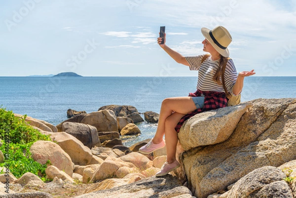 Fototapeta Woman is sitting on a rock and using video call
