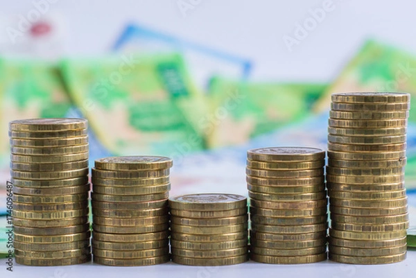 Fototapeta coins are neatly stacked in ascending order against blurred background vibrant banknotes. this scene represents financial growth and currency exchange, highlighting economic activities. close up.
