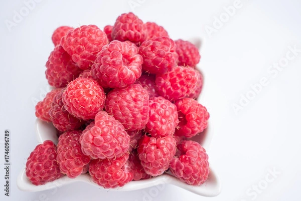 Fototapeta bowl filled with fresh raspberries showcases their bright red color and juicy texture. fruit is arranged neatly, emphasizing its appeal and freshness. close up.