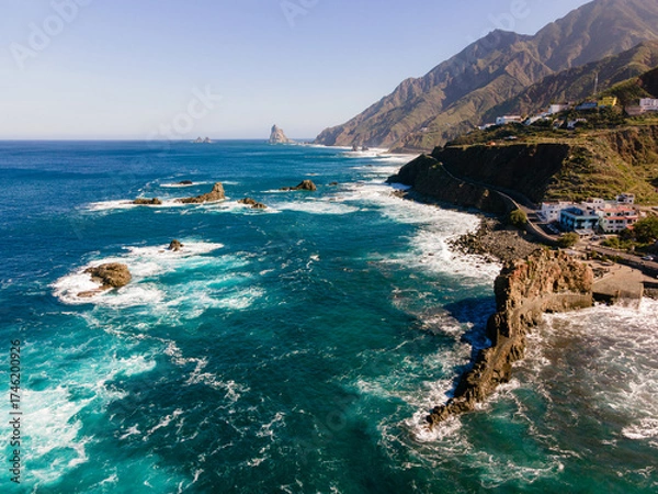 Fototapeta High angle aerial view of the rugged northern shoreline of Tenerife, Spain, with striking azure blue sea, dark volcanic rocks, and foamy waves creating vivid contrast.

