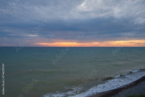 Fototapeta Orange sunset on the sea. Bright juicy landscape with feathery clouds on the horizon. Purple, lilac, pink shades of the evening sky. A calm turquoise sea rolls onto the beach. Idyll, relaxation