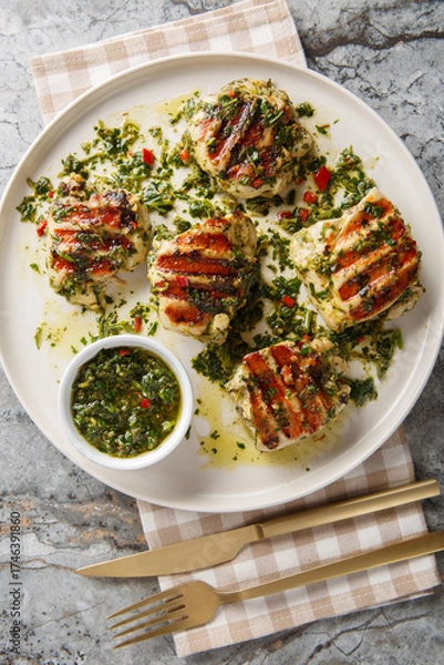 Obraz Grilled chicken thighs with Argentinian chimichurri sauce closeup on the plate on the table. Vertical top view from above