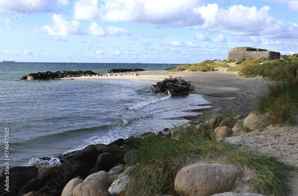 Fototapeta Landscape photo with a view of a bay of sea, a sandy beach with large stones in the foreground and a bunker on the coast at Cape Grenen, in Skagen, northern Denmark