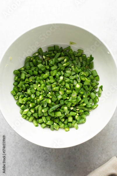 Fototapeta Overhead view of diced green beans, top view of green beans, sliced haricot verts on a white countertop, process of making nigerian fried rice