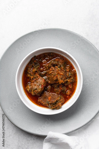 Fototapeta Overhead view of miyan taushe in a white bowl, top view of northern nigerian miyan taushe soup on a white countertop	