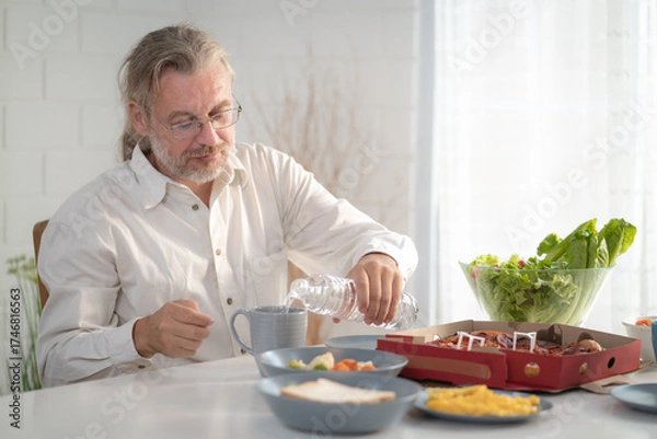 Fototapeta Senior elderly older grandfather stay at home with painful face sitting alone on eating table in house. Depressed elderly retired man upset feeling unhappy. Lonely and missing his family at home	
