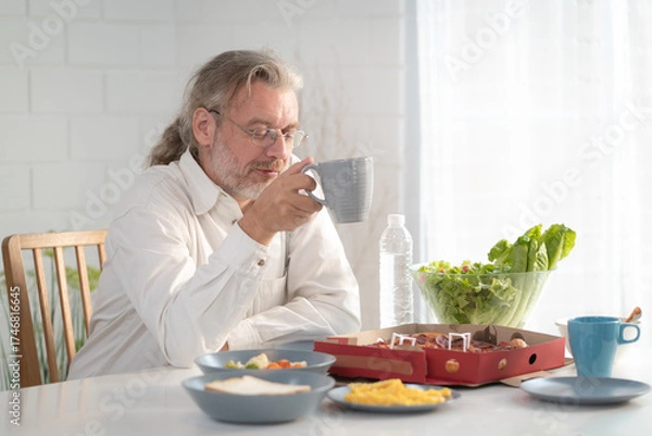 Fototapeta Senior elderly older grandfather stay at home with painful face sitting alone on eating table in house. Depressed elderly retired man upset feeling unhappy. Lonely and missing his family at home	