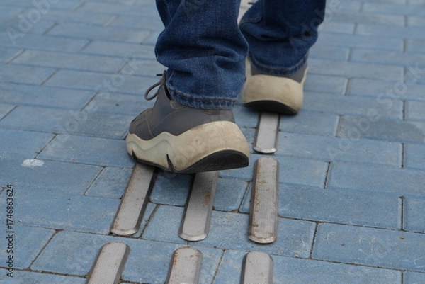 Fototapeta Feet Walking on Tactile Guiding Strips: Close-up of Accessibility Paving