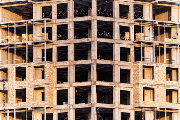 Fototapeta A detailed close-up shot of a modern residential or commercial building under construction. The concrete skeleton and exposed brick walls form a symmetrical grid of windows and structural elements.