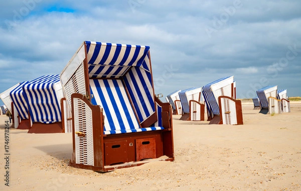 Fototapeta Typical beach chairs with blue and white striped cushions on the sandy beach of Norderney invite you to relax and sunbathe. A vacation idyll on the North Sea (Germany)