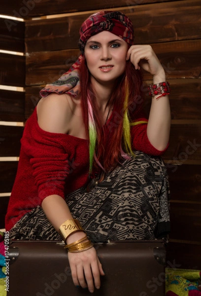 Fototapeta Cheerful hippie boho redhead woman poses with old suitcase on a wooden wall background