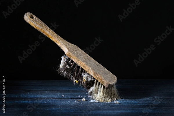Fototapeta Old hand brush with worn wooden handle and natural bristles with many dust bunnies, standing against a dark background, still life, vintage cleaning utensil, copy space, selected focus