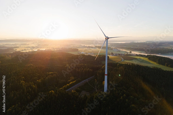 Fototapeta Wind Turbine at Sunrise Over Forest and Farmland