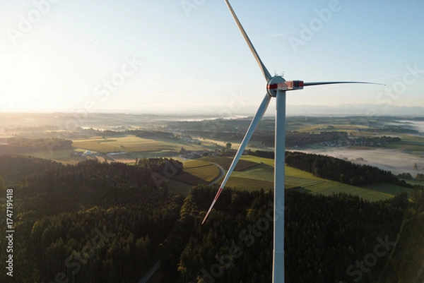 Fototapeta Wind Turbine at Sunrise Over Forest and Farmland