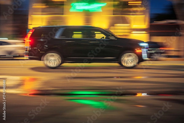 Fototapeta Black executive limo SUV car driving along illuminated wet street at night. Long exposure. Bright colorful neon city lights blurred in background