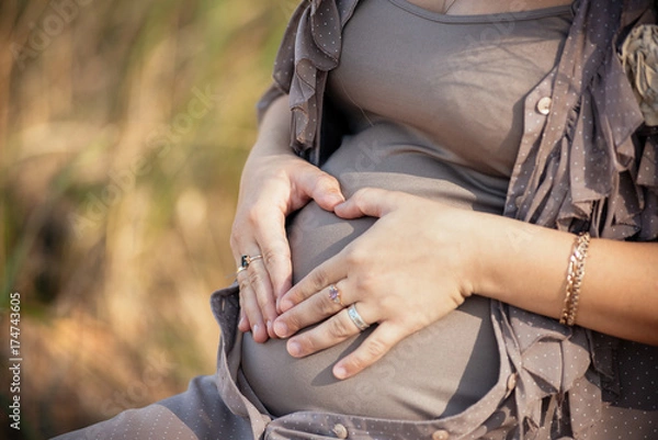 Fototapeta hands of a beautiful pregnant girl, folded on the belly in the shape of a heart. Love for children