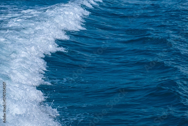 Fototapeta Dark blue and white ocean waves form diagonal lines on the sea surface, with fine white foam contrasting against the rippling water, demonstrating the power and movement of the ocean.