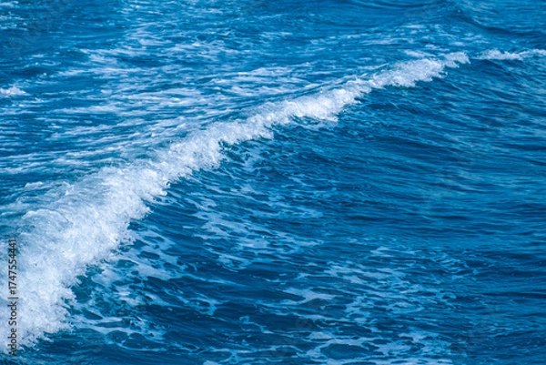 Fototapeta Dark blue and white ocean waves form diagonal lines on the sea surface, with fine white foam contrasting against the rippling water, demonstrating the power and movement of the ocean.